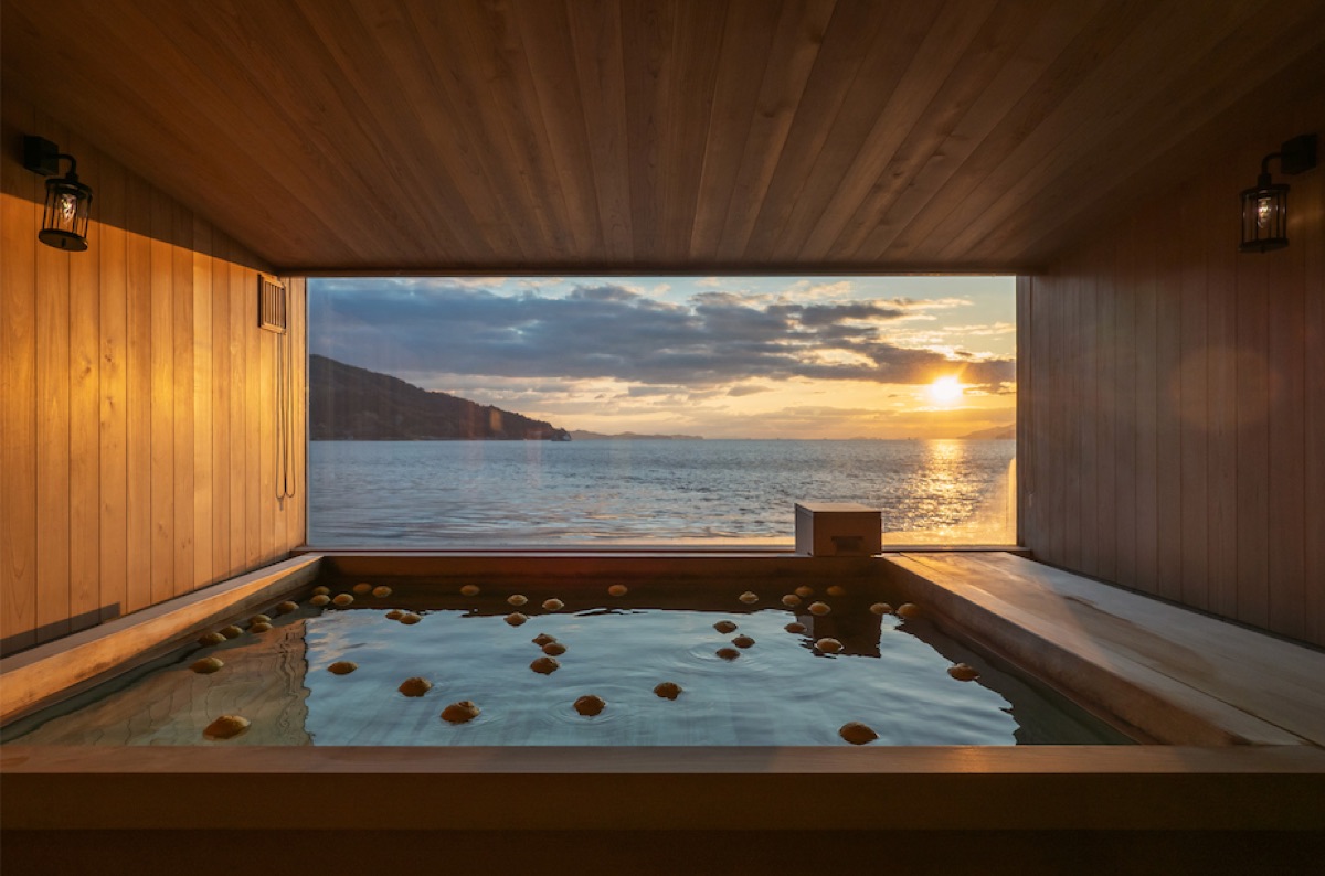A wooden bath aboard guntu with citrus floating in the water, open to the Seto Inland Sea at sunset