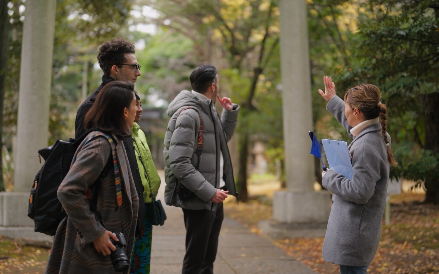 A guide talking with a small group of guests on a tree-lined shrine path